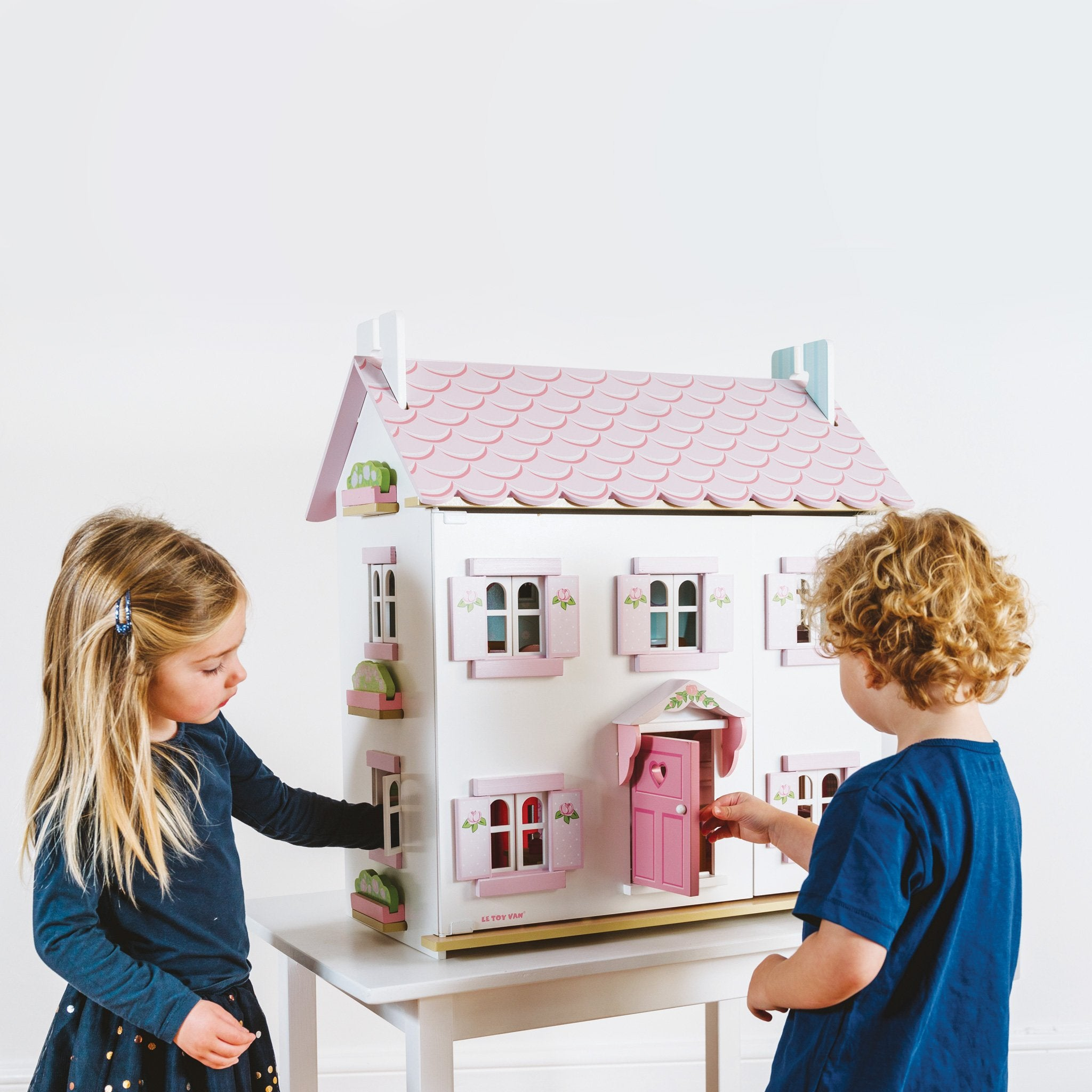 Zwei Kinder spielen mit einem Puppenhaus. Ein Mädchen schaut hinein, ein Junge öffnet die Tür.