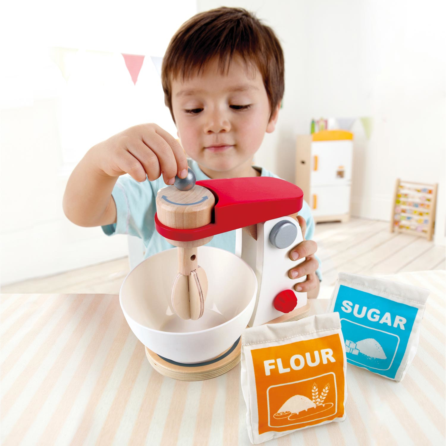 Ein Junge spielt mit einem Spielzeugmixer, einer Schüssel, Mehl und Zuckerbeuteln.
