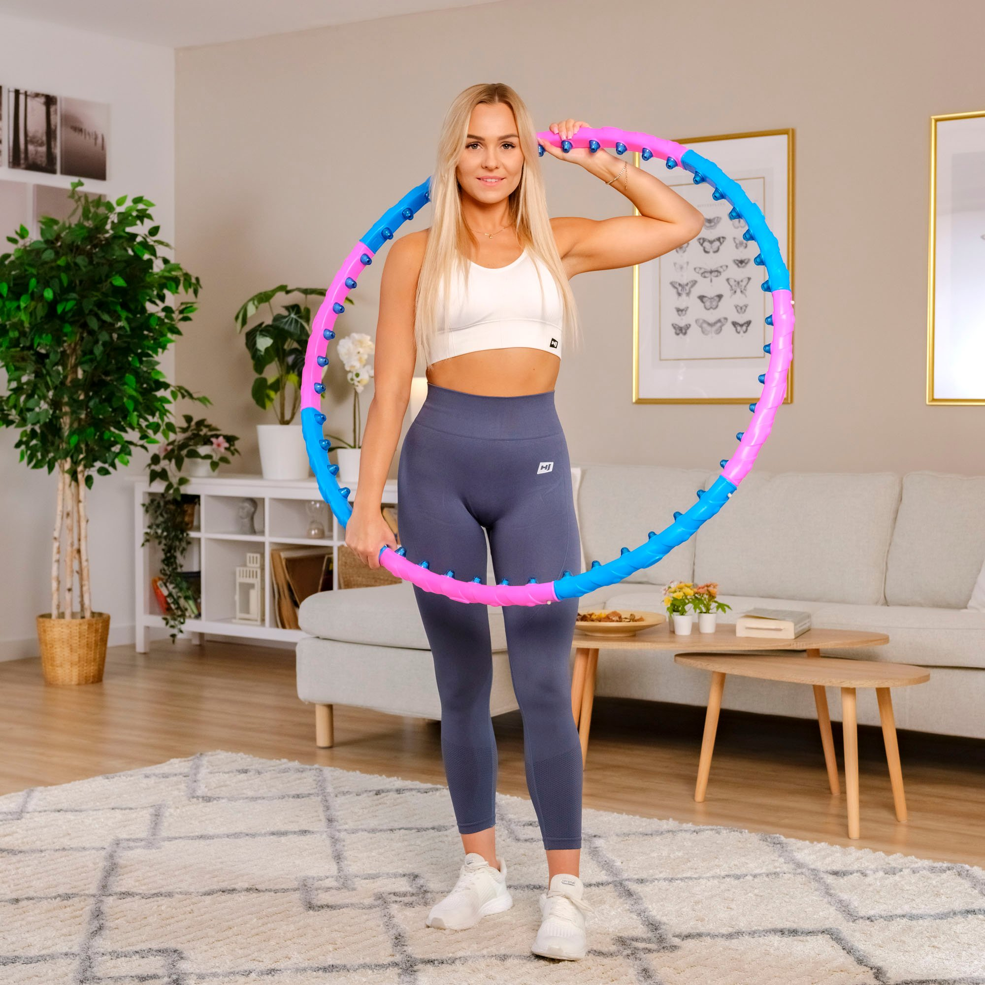 Eine Frau hält einen rosa-blauen Hula-Hoop-Reifen in einem Wohnzimmer.
