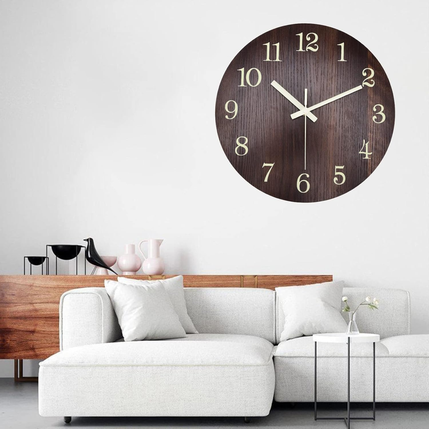 Eine dunkle Holz-Uhr mit weißen Ziffern hängt über einem weißen Sofa mit Kissen.