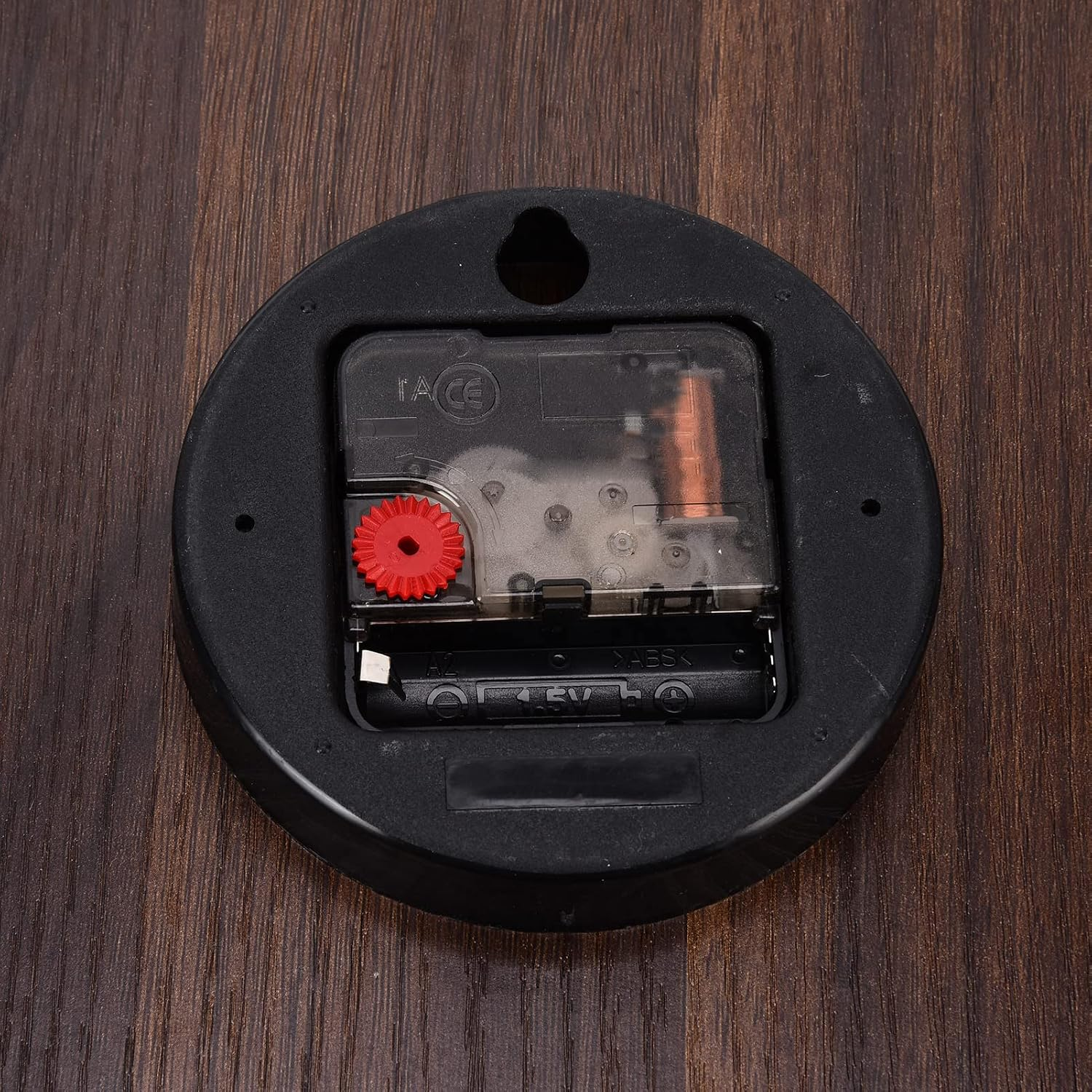 Rückseite einer Uhr mit Uhrwerk, Batteriefach und rotem Einstellrad auf Holzoberfläche.