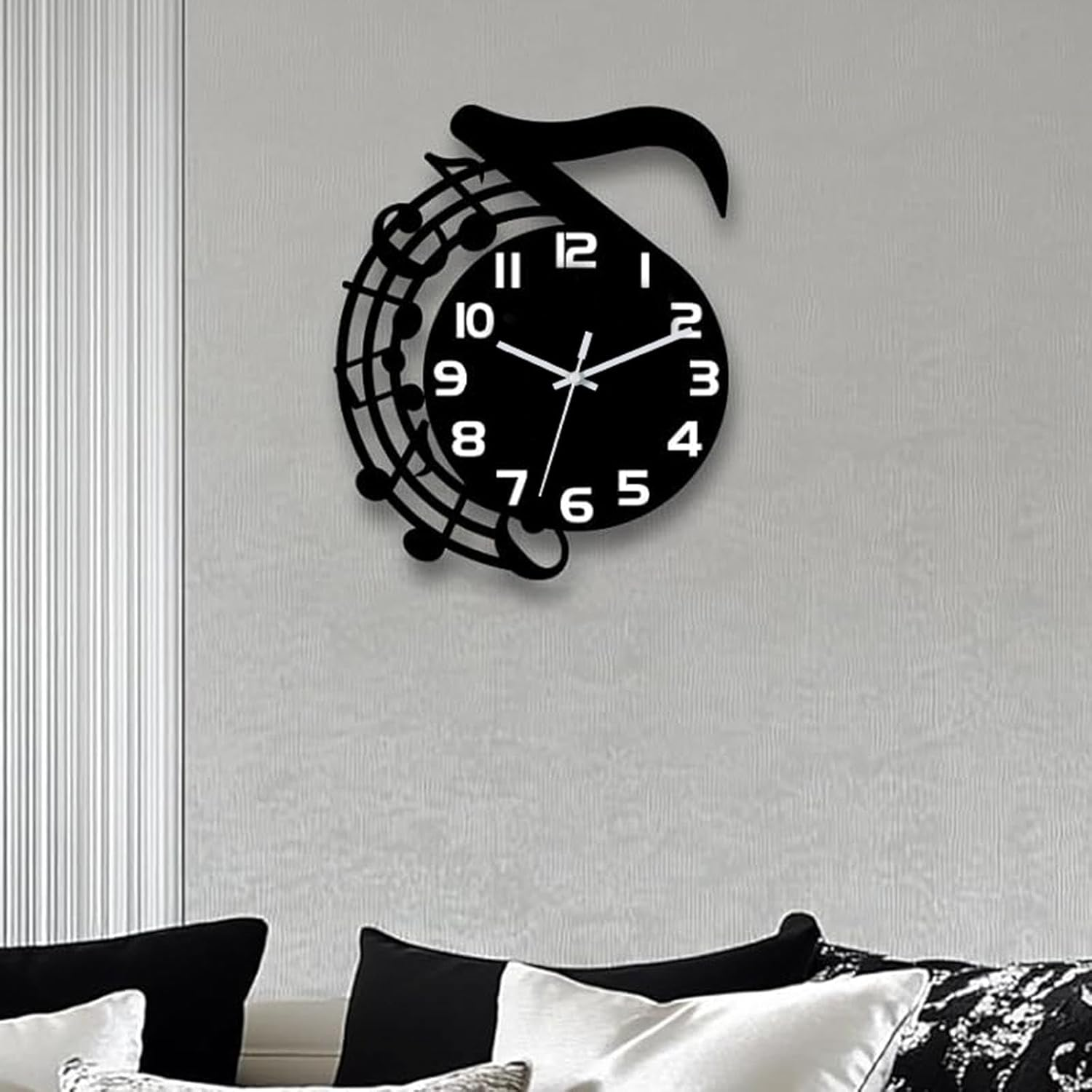 Eine schwarze Wanduhr im Musiknoten-Design hängt an einer grauen Wand über Sofakissen.
