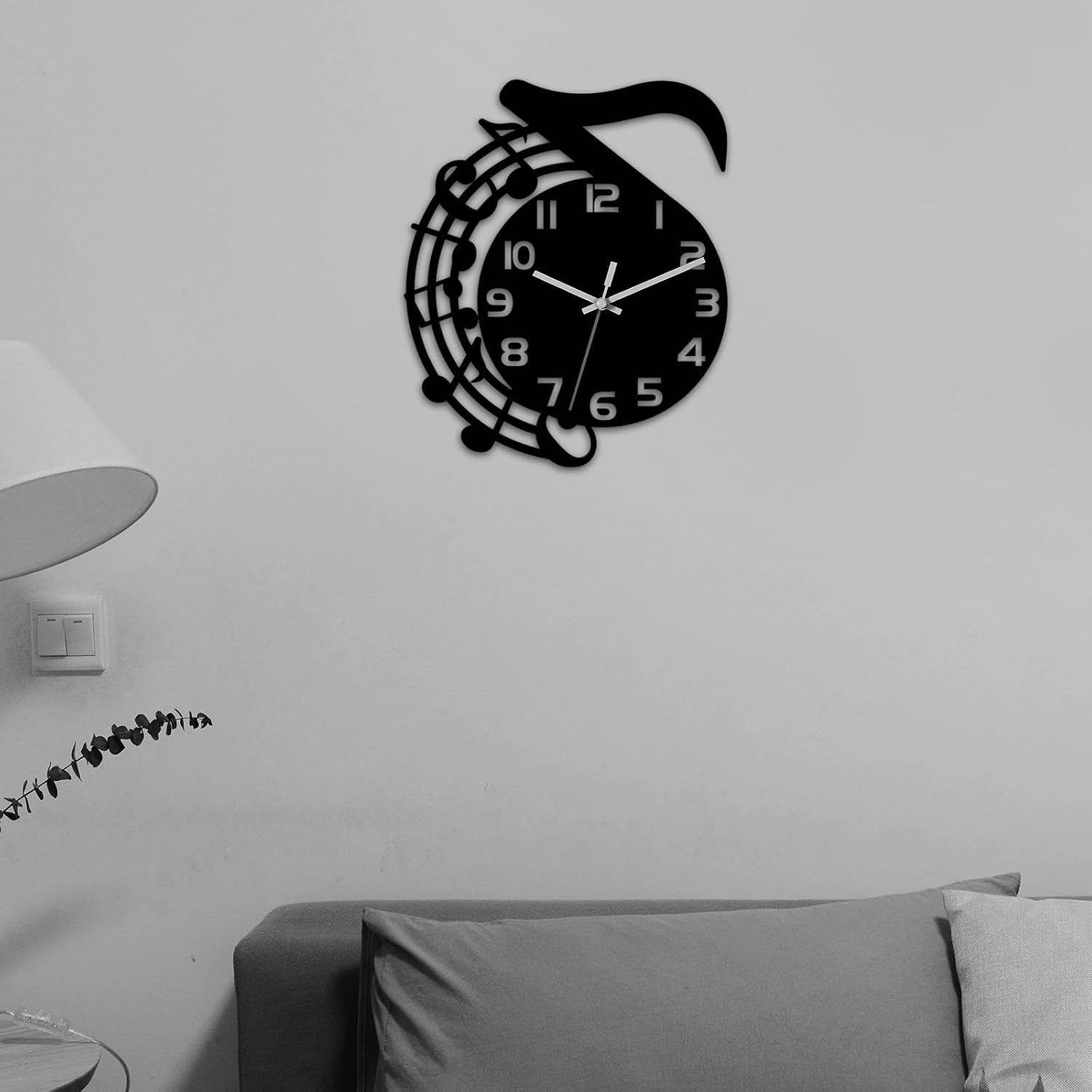 Eine schwarze Wanduhr im Notenschlüssel-Design hängt an einer weißen Wand.