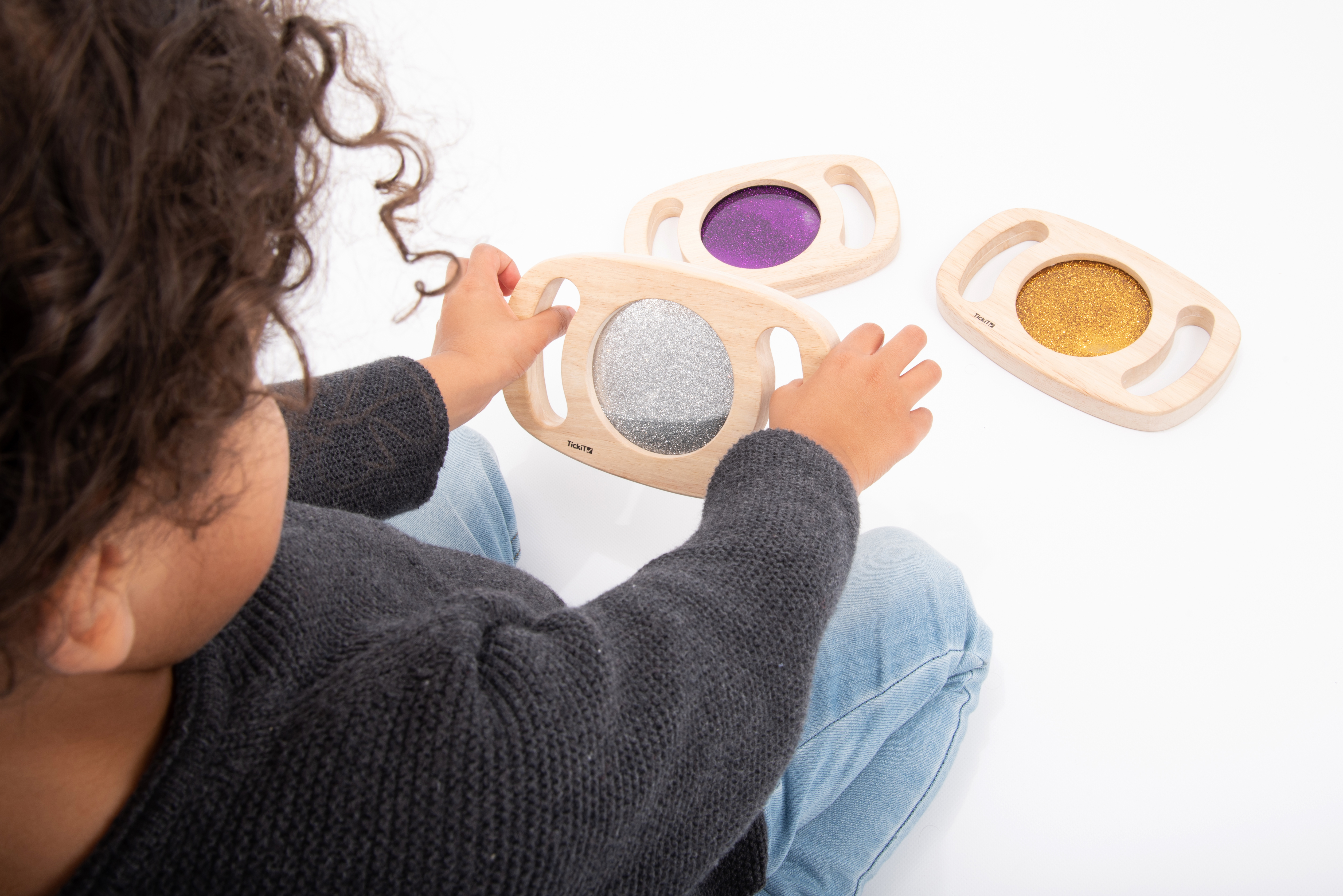 Un niño juega con tres marcos de madera con brillantina: plateada, morada y dorada.