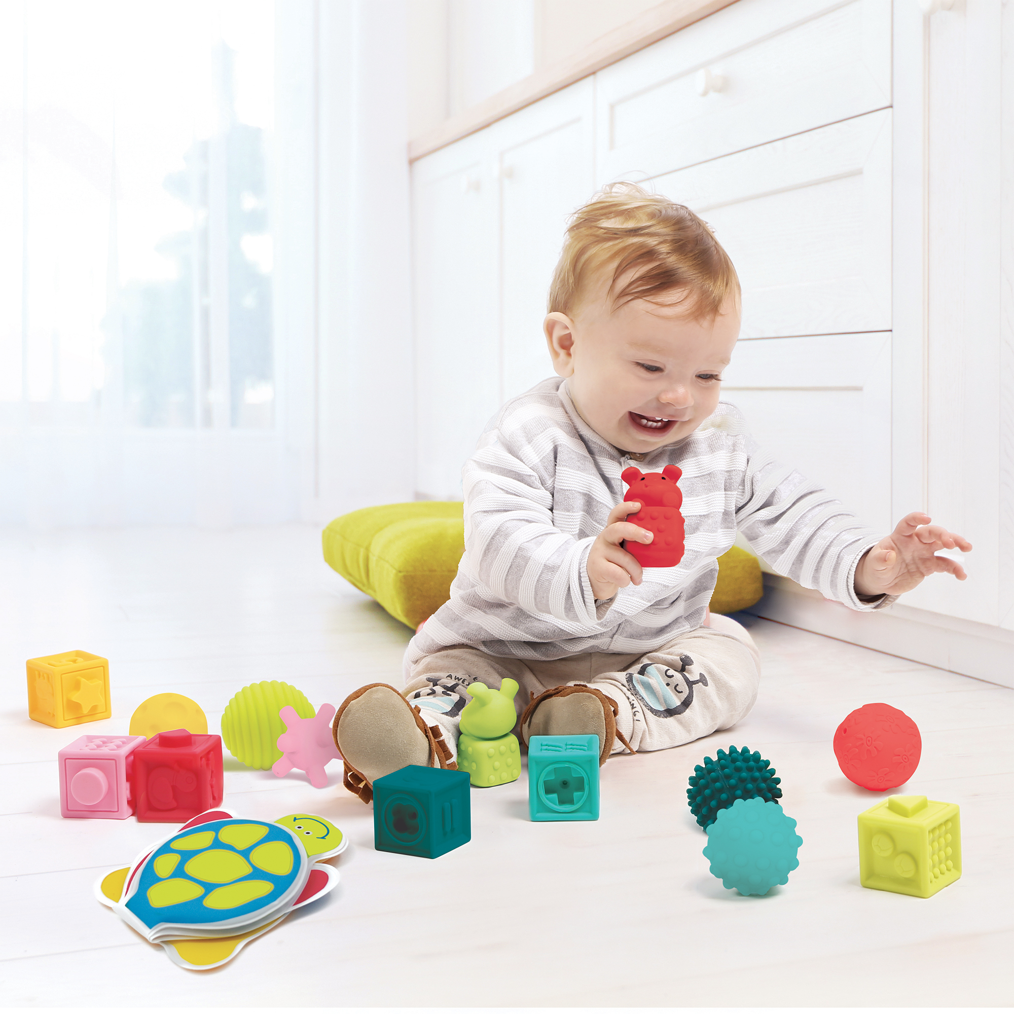 Ein Baby spielt mit bunten Beißspielzeugen auf dem Boden.