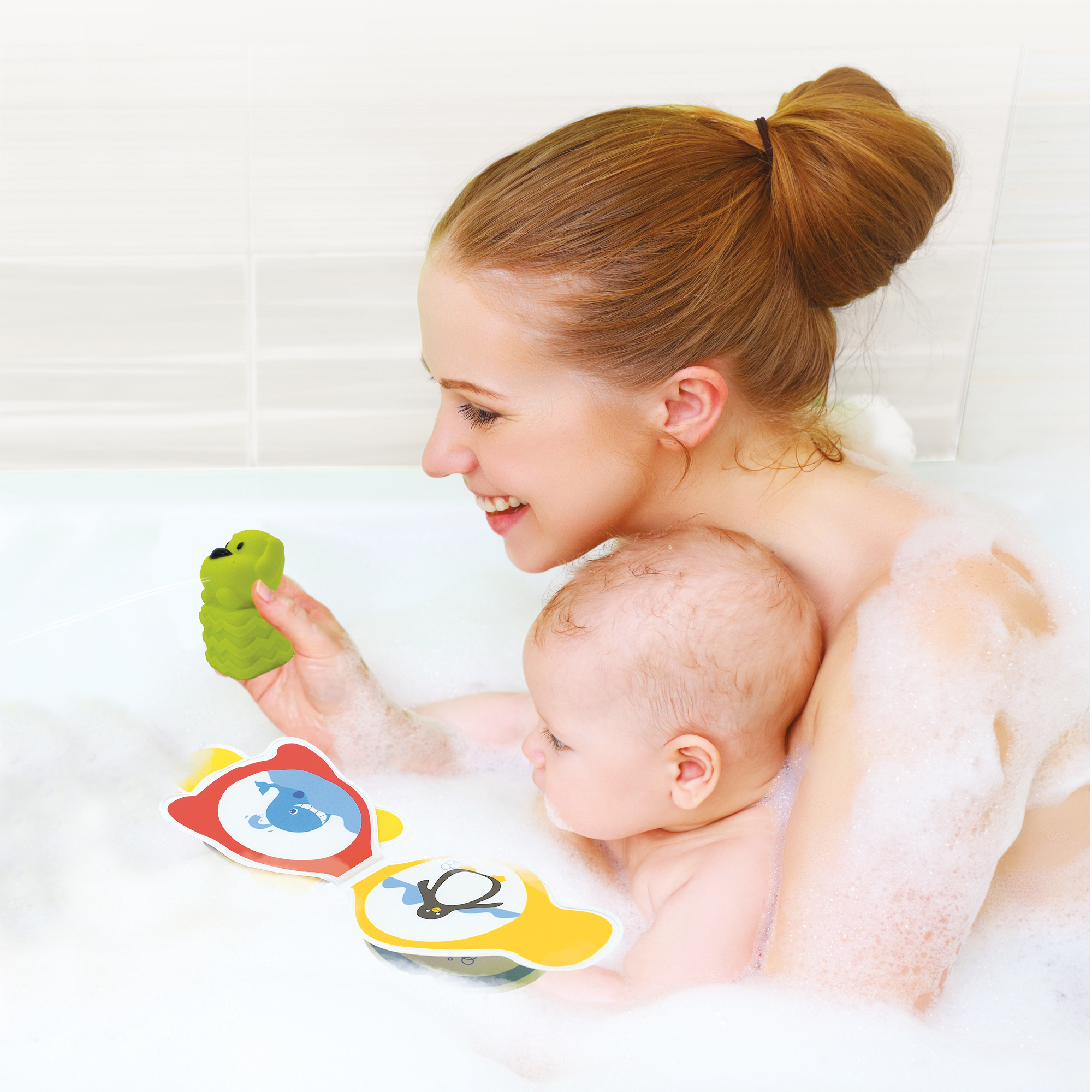 Eine Frau hält ein grünes Spielzeug, während ein Baby in der Badewanne spielt.