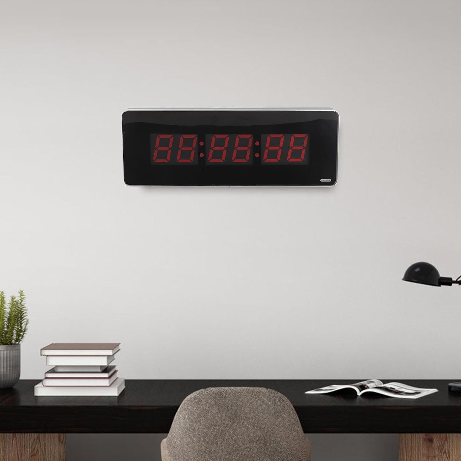 Eine große Digitaluhr mit roten Ziffern hängt an einer weißen Wand über einem Schreibtisch.