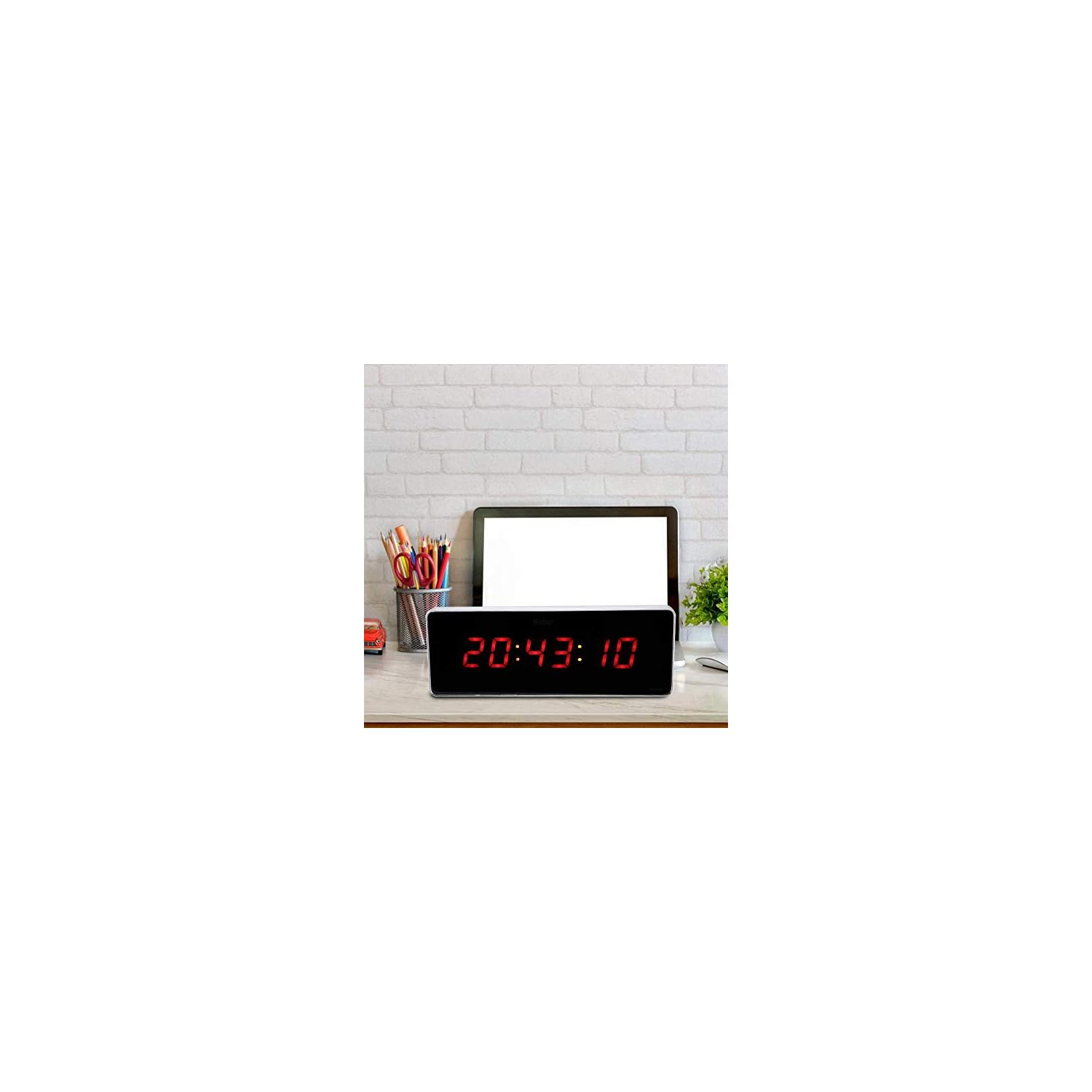 Digitaluhr zeigt 20:43:10 auf einem Schreibtisch mit Stiften und Laptop.
