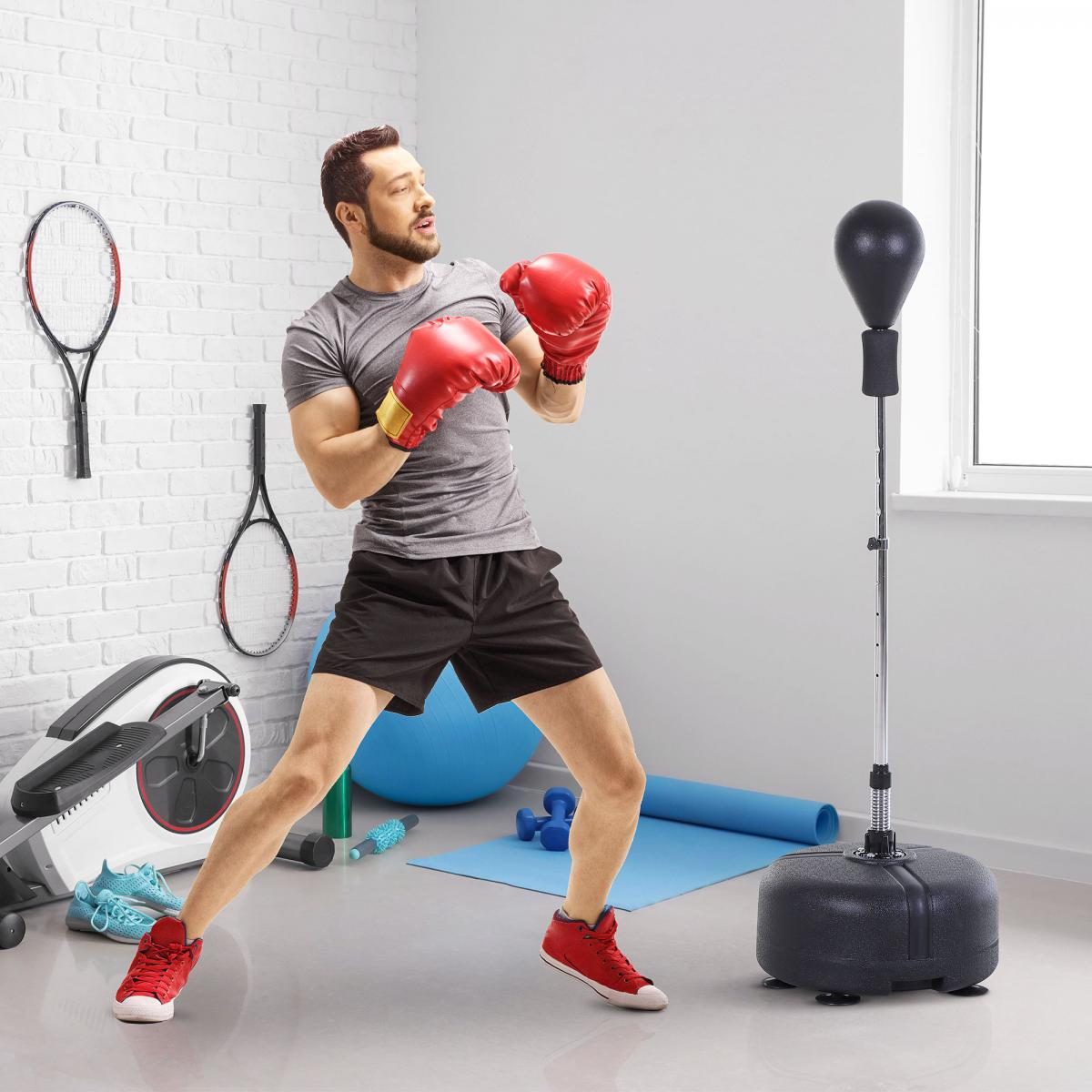 Ein Mann mit roten Boxhandschuhen trainiert an einem Boxsack. Tennisschläger an der Wand.