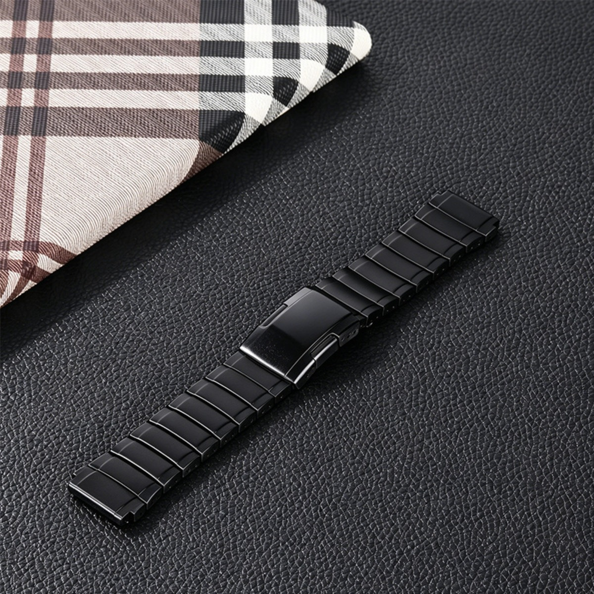 Ein glänzendes schwarzes Uhrenarmband aus Metall mit Gliedern und einer Schnalle auf schwarzem Leder.