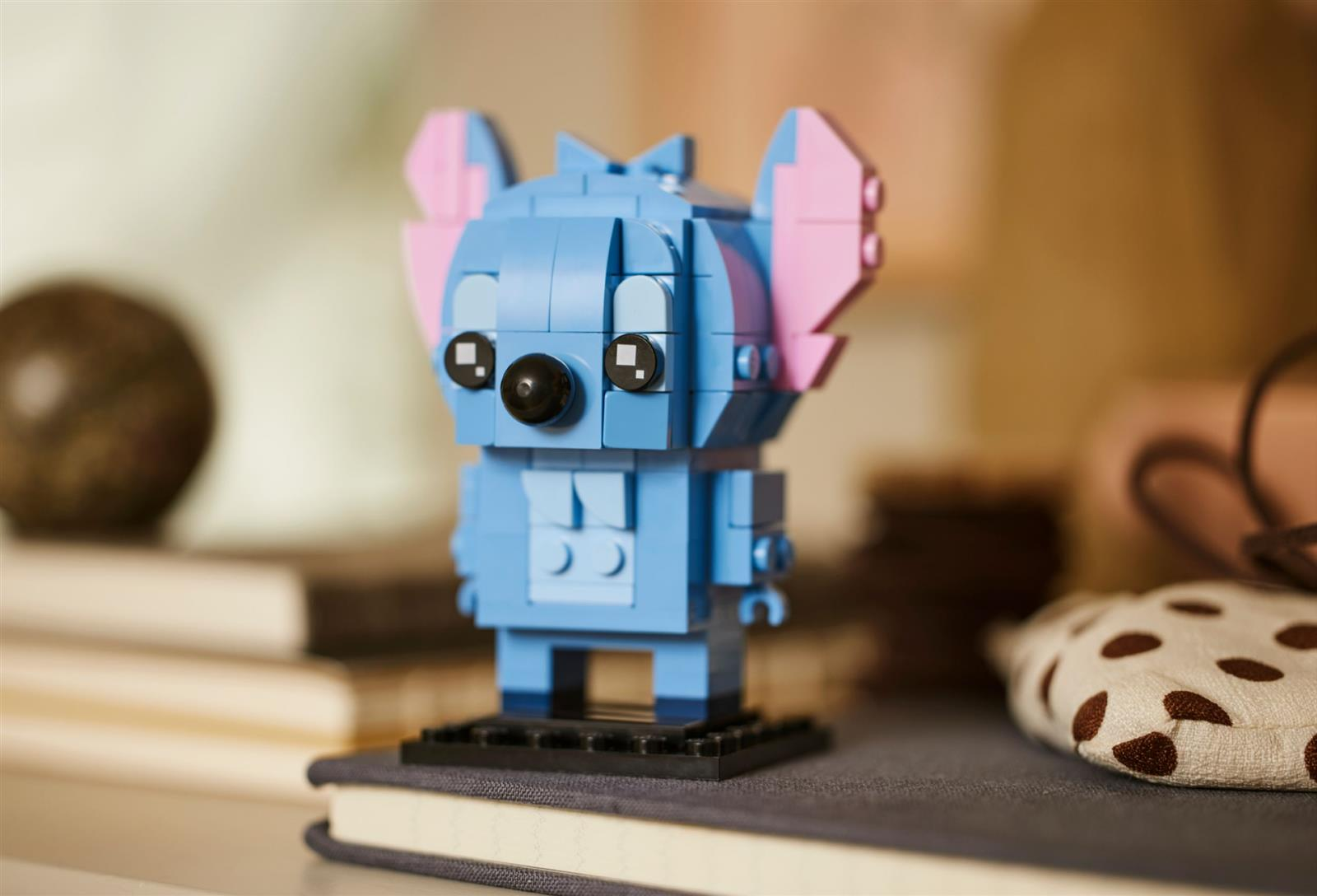 Ein blauer Lego-Stitch mit rosa Ohren steht auf einem Buch. Daneben sind Objekte.
