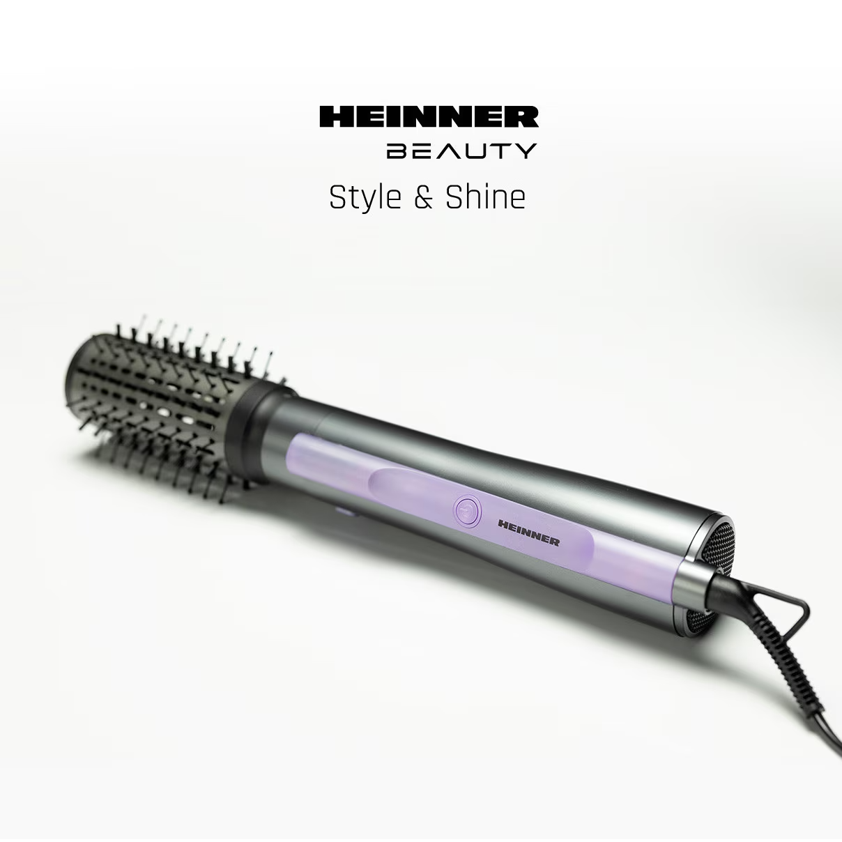 Un sèche-cheveux foncé avec brosse et accents violets repose sur une surface blanche.