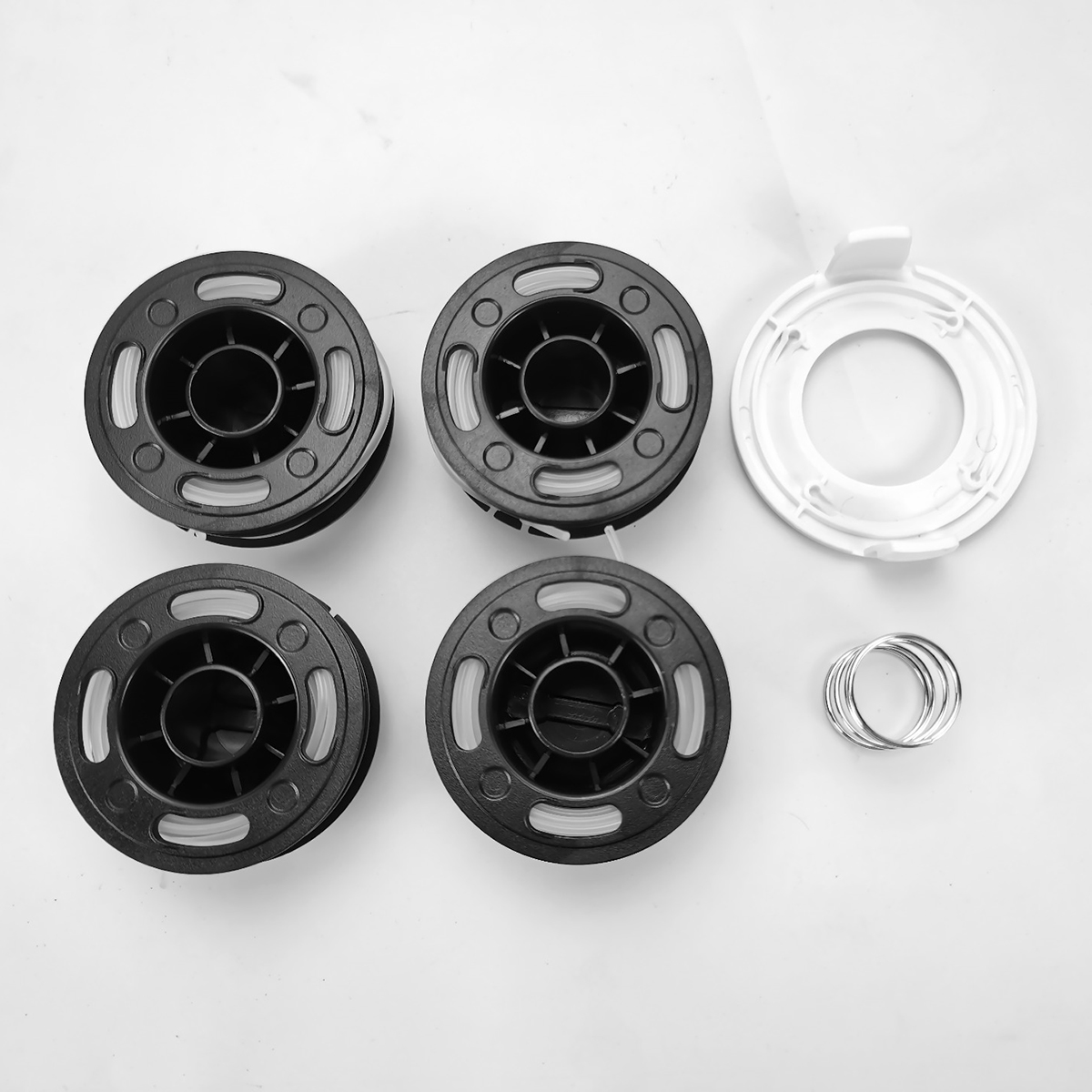 Vier schwarze Schnurspulen, eine weiße Spulenabdeckung und ein Stapel Metallringe auf weißer Fläche.
