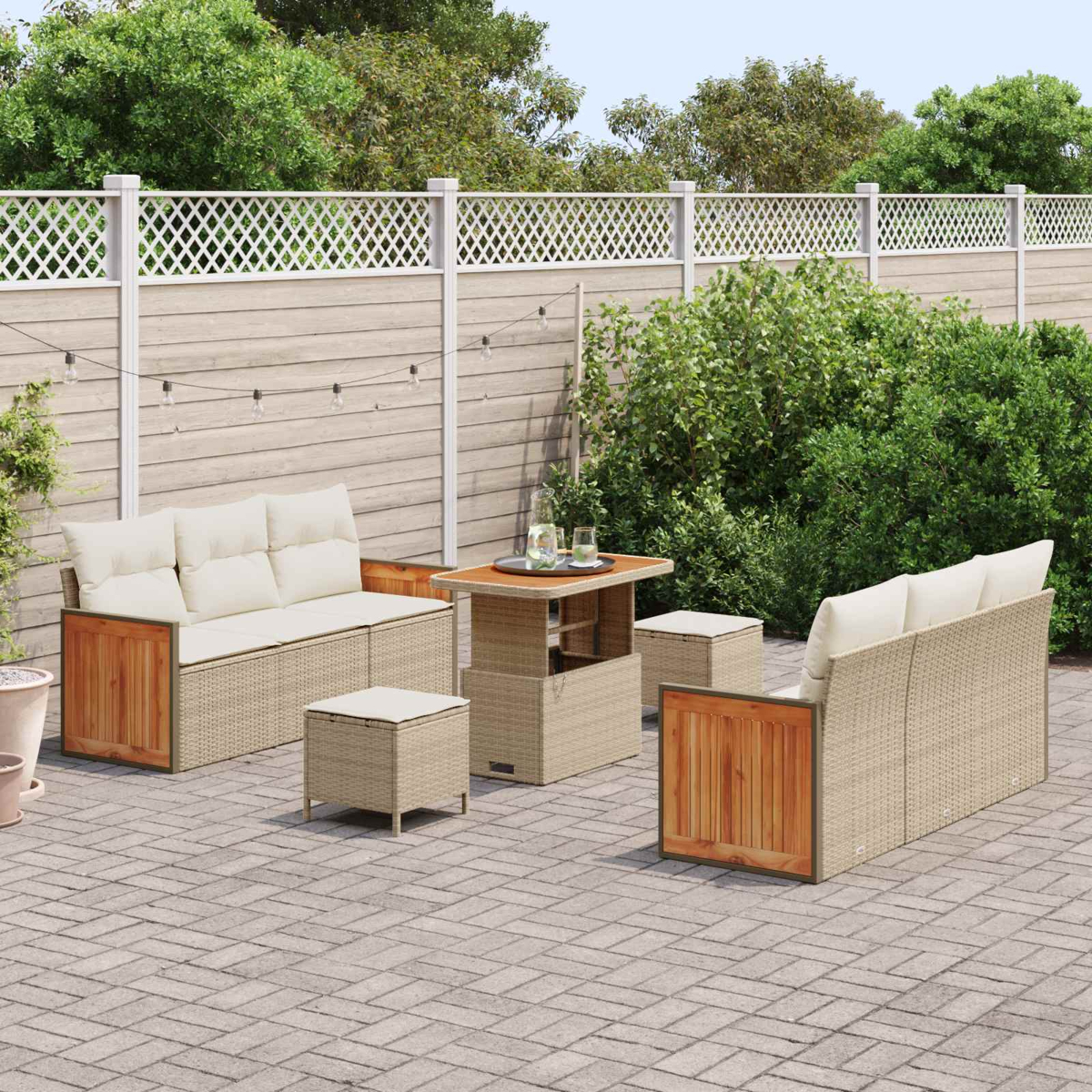 Geflochtene Gartenmöbel mit Kissen auf einer Steinpflasterterrasse mit Holzzaun und Bäumen.