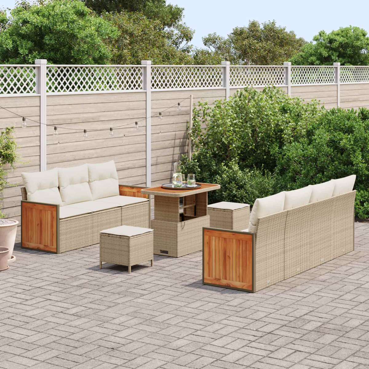Gartenlounge mit Rattansofa, Tisch und Hockern auf gepflasterter Terrasse.