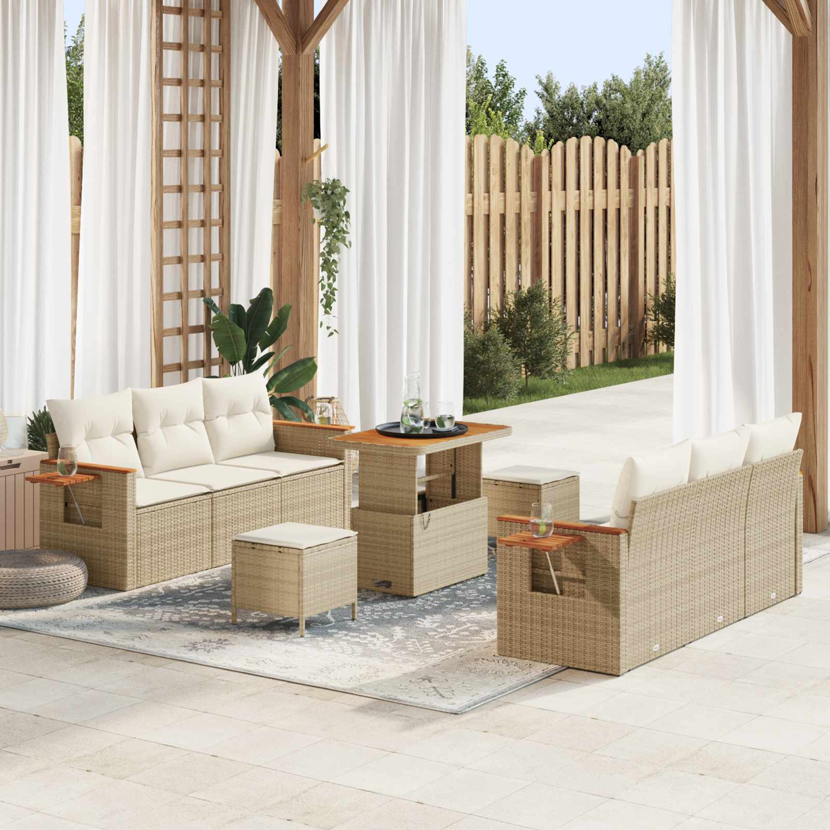 Geflochtene Gartenmöbel mit weißen Kissen auf einer Terrasse mit Holzzaun und Vorhängen.