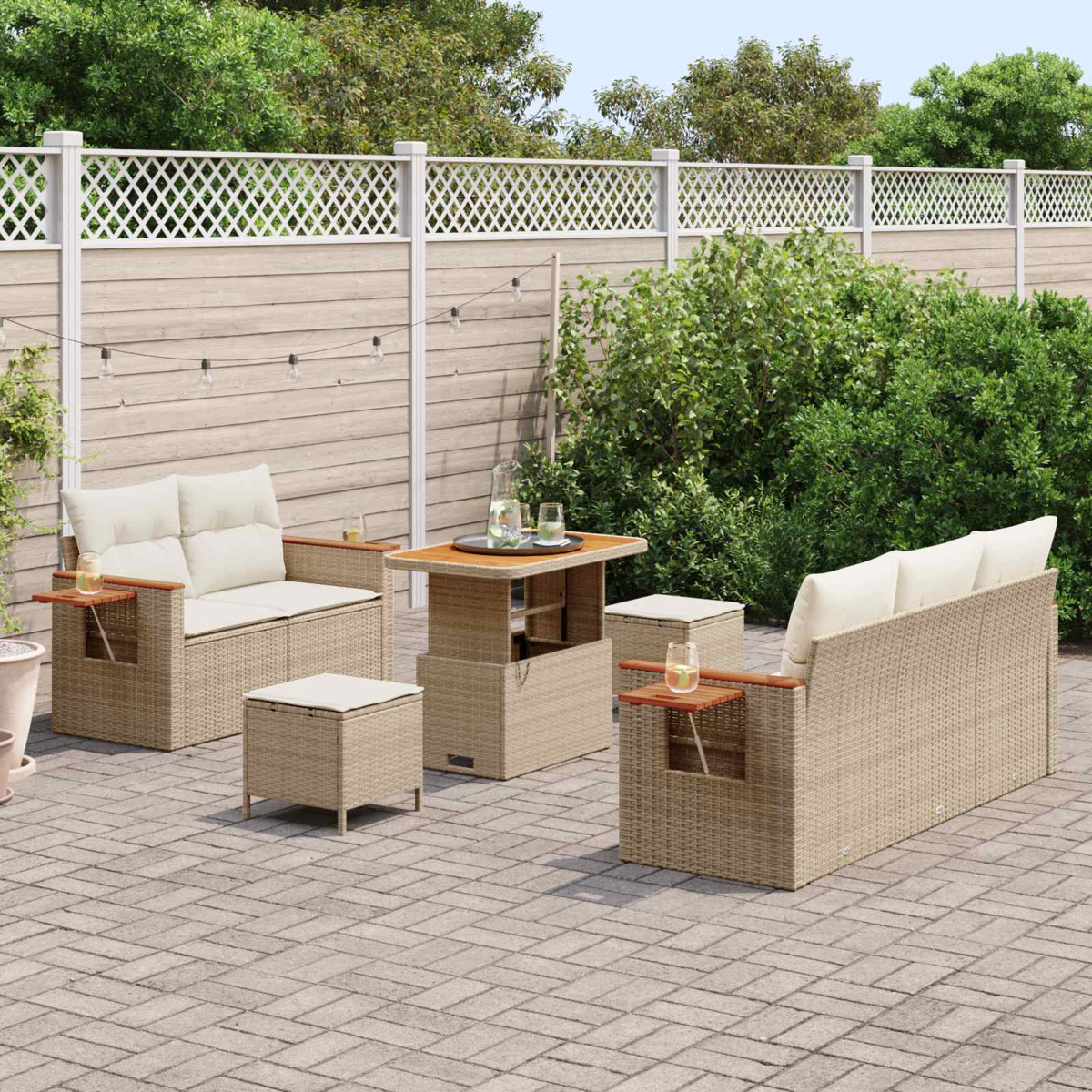 Beiger Rattansofa mit Kissen, Tisch und Hockern auf einer gepflasterten Terrasse.