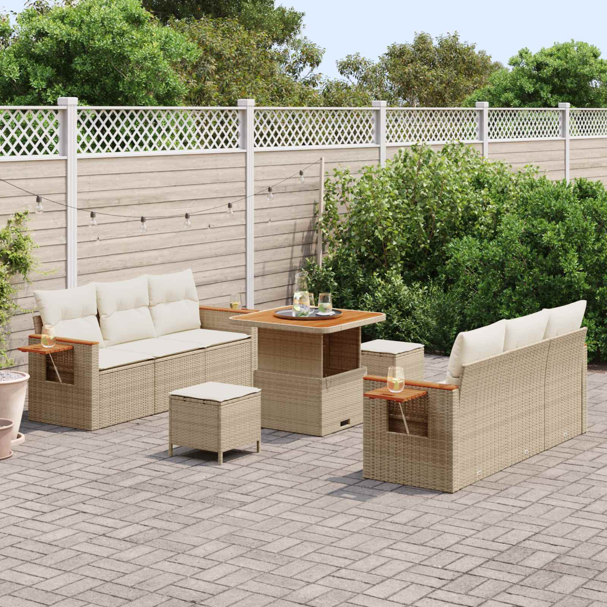 Ein beigefarbenes Korbgeflecht-Terrassenmöbelset mit Sofas, Tisch und Hockern auf einer gepflasterten Terrasse.