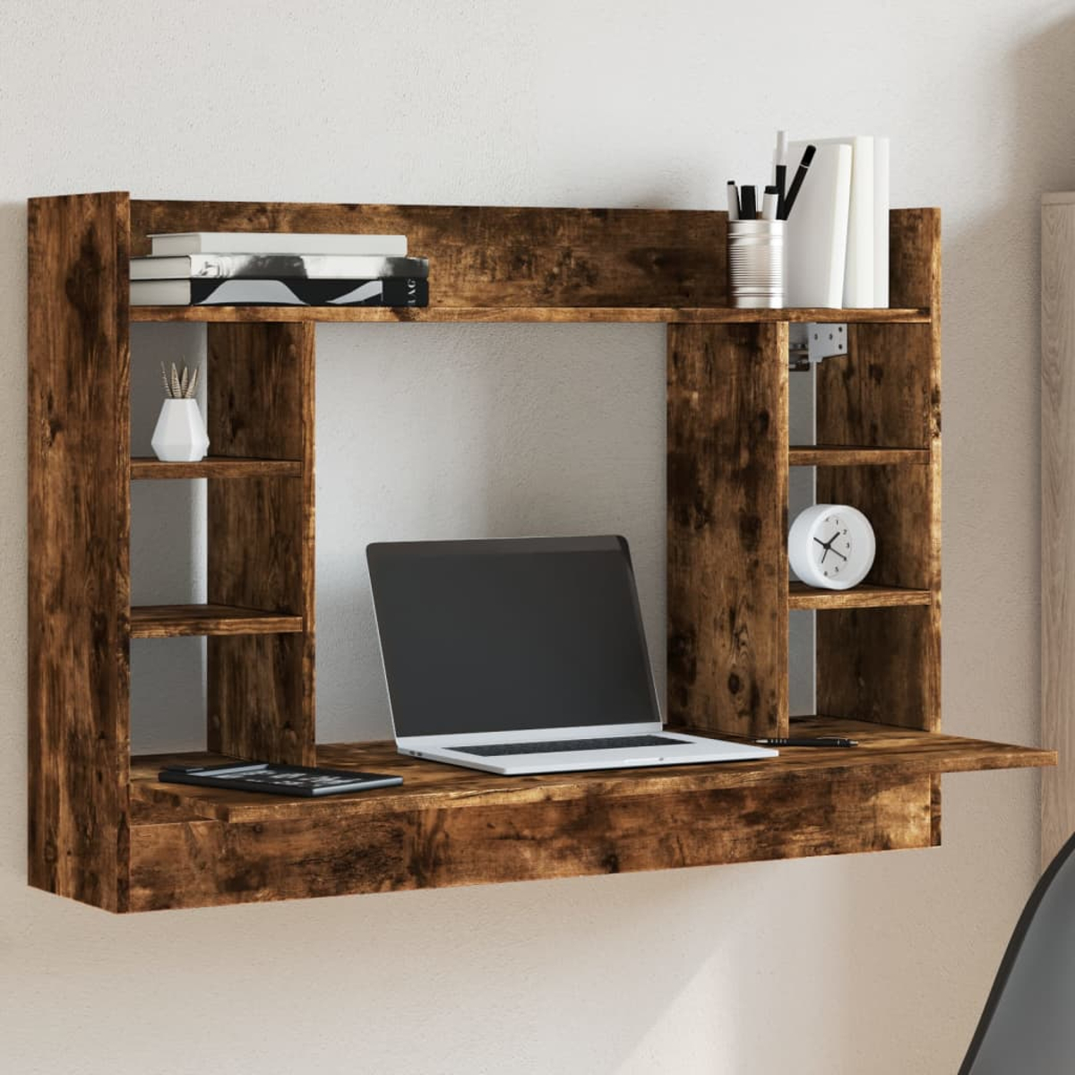 Ein rustikaler Holztisch mit Laptop, Büchern, Vase, Uhr und Stiften an einer weißen Wand.