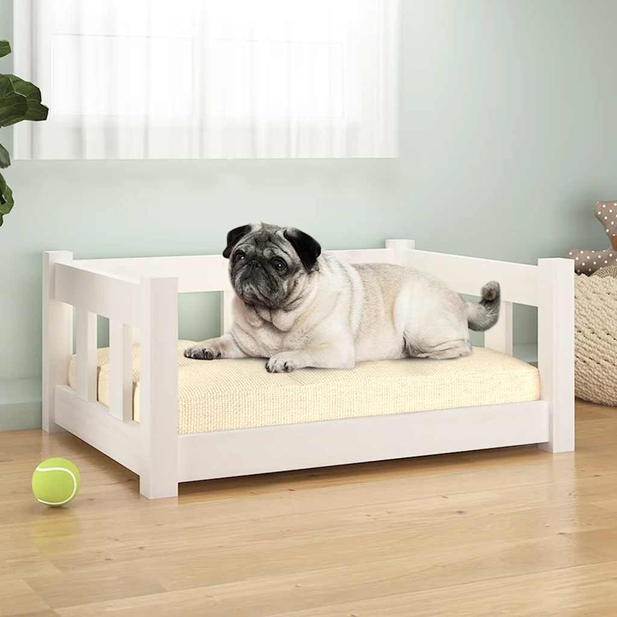 Ein Mops ruht auf einem weißen Hundebett mit gelbem Kissen. Ein Tennisball liegt am Boden.
