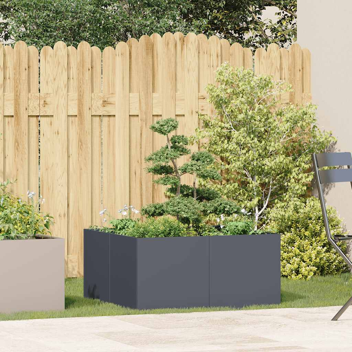 Una fioriera rettangolare grigio scuro con piante e un albero davanti a una recinzione di legno.