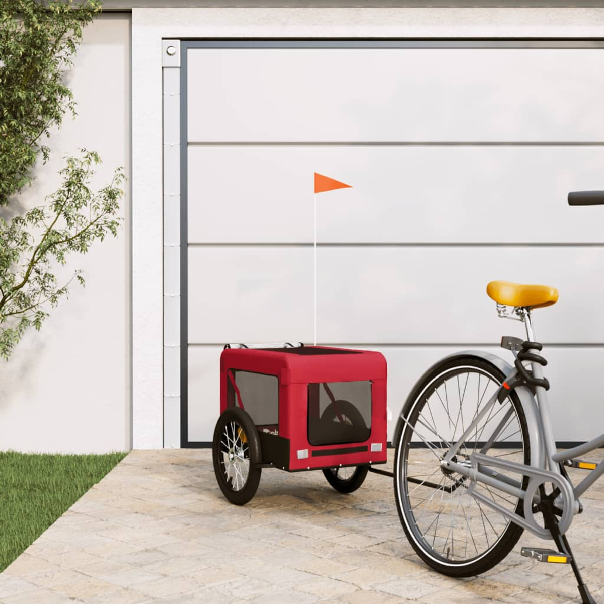Ein roter Fahrradanhänger mit Orangenflagge neben einem Fahrrad vor einer Garage.