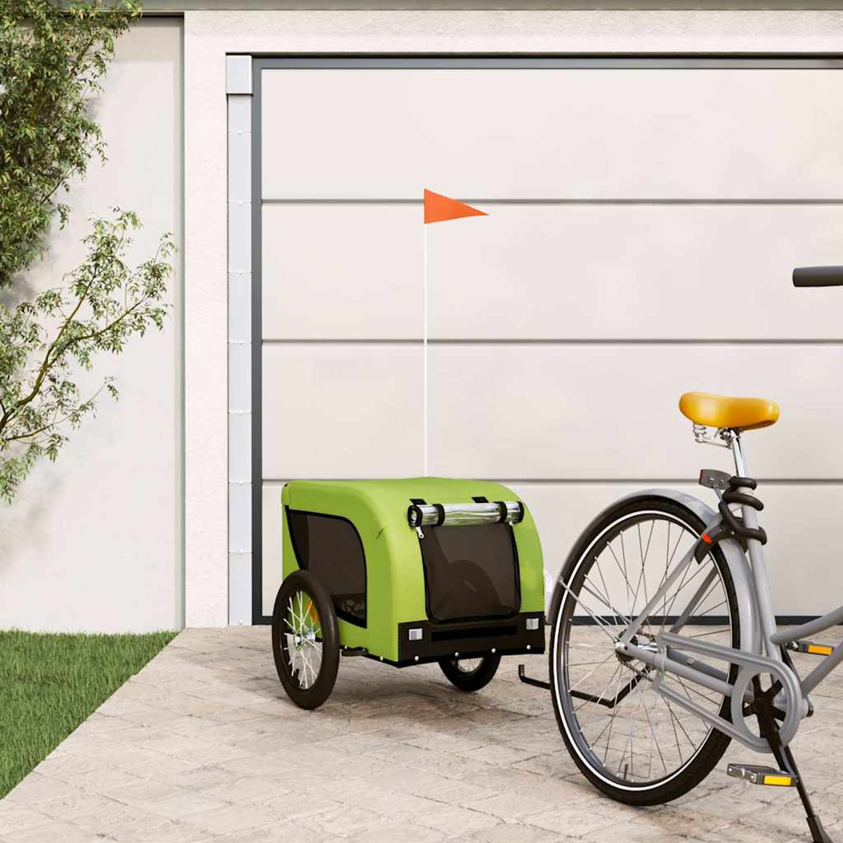 Ein grüner Fahrradanhänger mit orangem Fähnchen steht neben einem Fahrrad vor einer Garagentür.