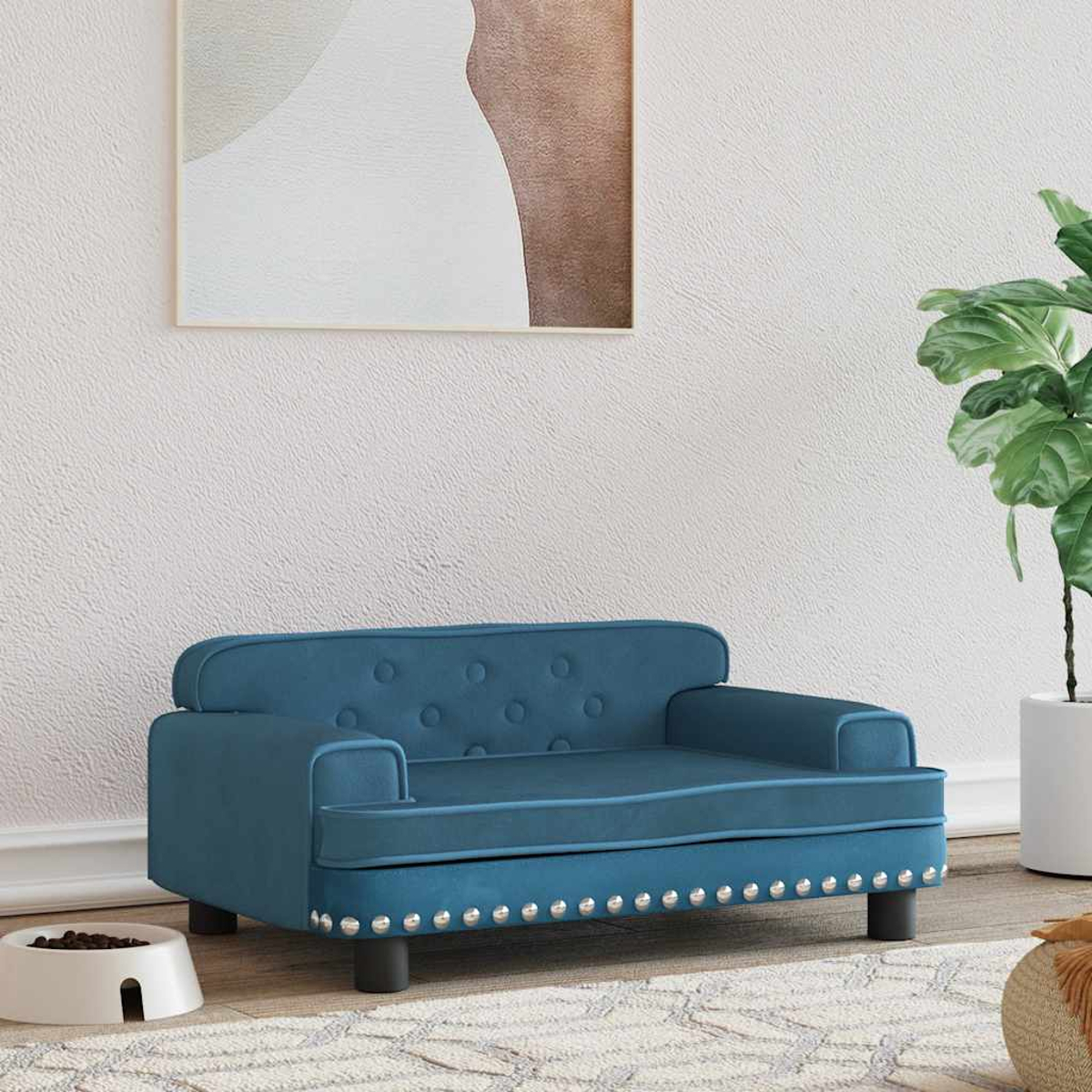 Blaue, getuftete Haustiercouch mit silbernen Nagelkopfleisten, vor weißer Wand und abstrakter Kunst.