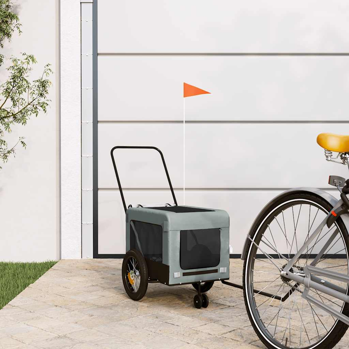 Ein grauer Fahrradanhänger mit orangefarbener Fahne steht neben einem Fahrrad.