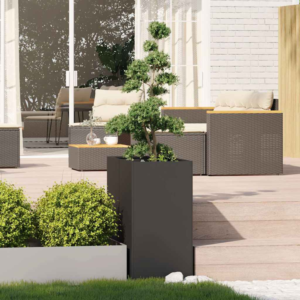 Un patio moderno con mobili in vimini grigio scuro, un bonsai in un vaso e arbusti verdi.