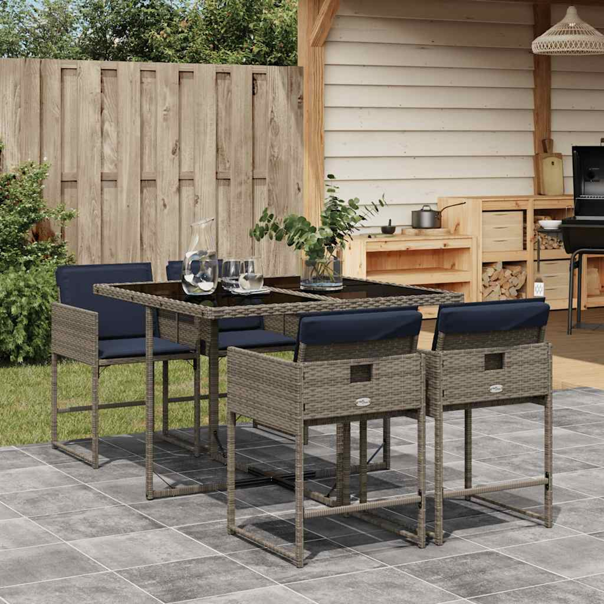 Ein Rattan-Gartentisch mit vier Stühlen, mit blauen Kissen, auf einer Steinterrasse.