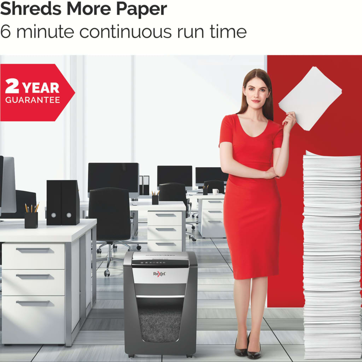 Kobieta w czerwonej sukience stoi obok niszczarki, biurka i sterty papieru.