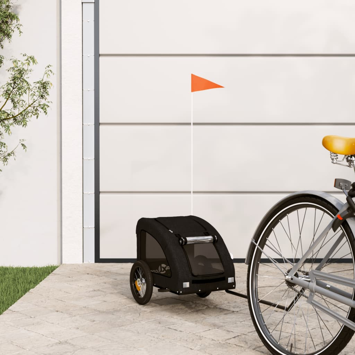 Ein schwarzer Fahrradanhänger mit orangem Wimpel steht neben einem Fahrrad.