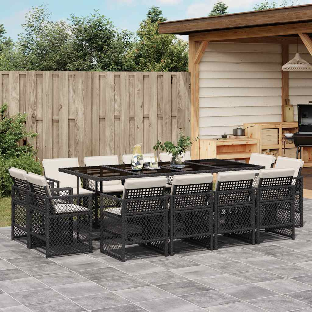 Ein dunkles Geflecht-Esstisch-Set mit acht Stühlen und Kissen steht auf einer gefliesten Terrasse.