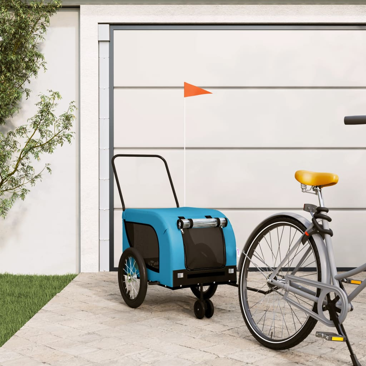 Ein blauer Fahrradanhänger mit orangefarbener Fahne neben einem Fahrrad vor einem Garagentor.