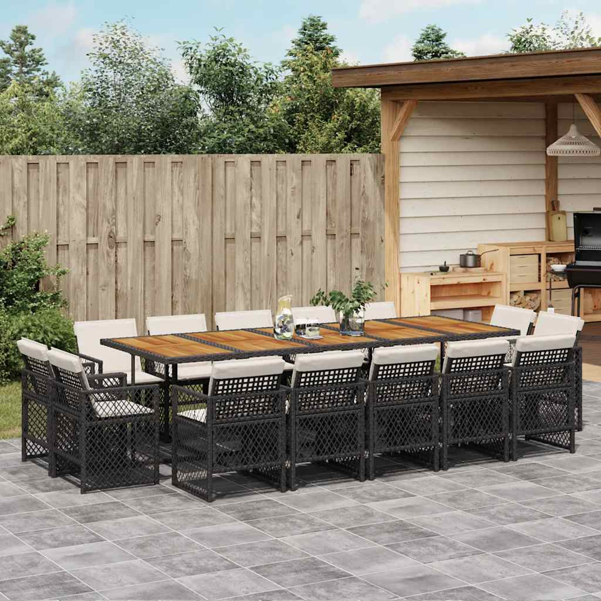 Essgruppe im Freien mit Holztisch, schwarzen Stühlen und Kissen. Terrasse mit Zaun und Schuppen.