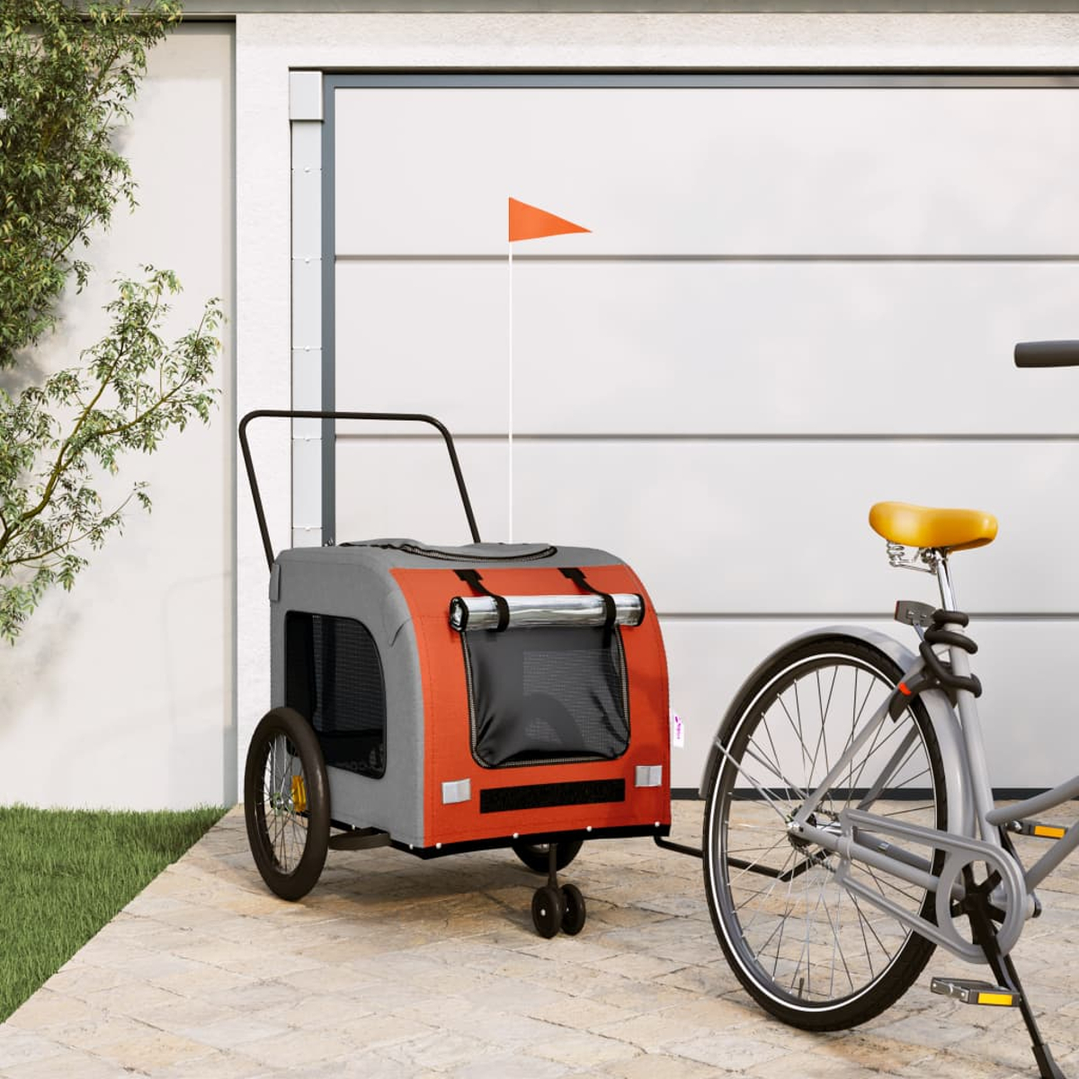 Ein Hundefahrradanhänger mit orangefarbener Front und grauen Seiten steht neben einem Fahrrad vor einem Garagentor.