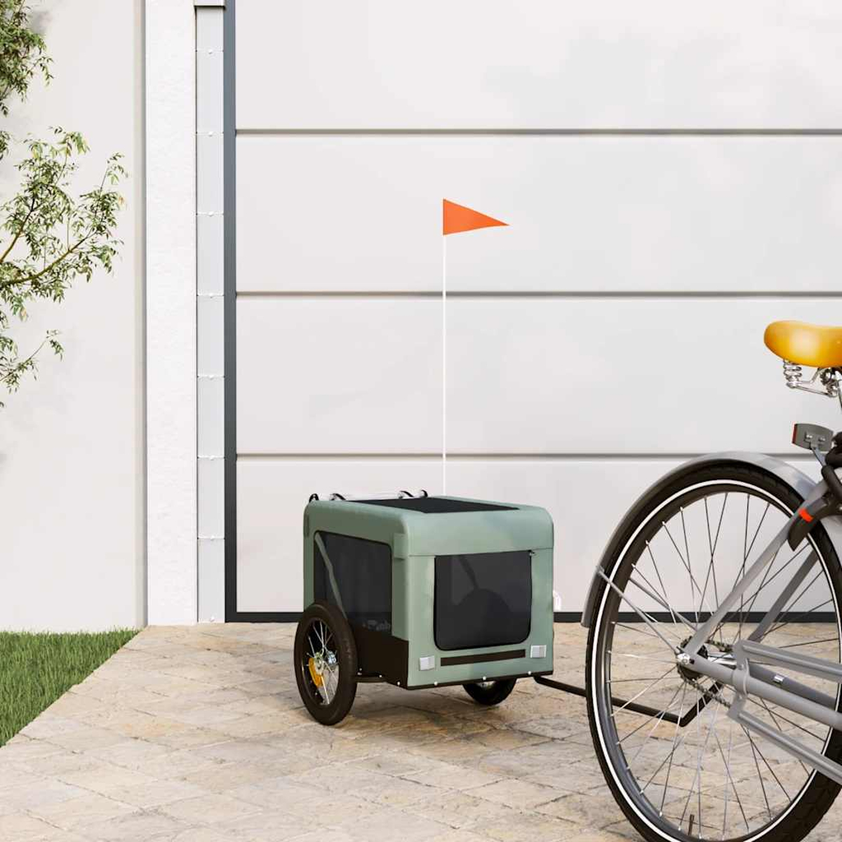 Ein grüner Fahrradanhänger mit orangefarbener Flagge neben einem Fahrrad.