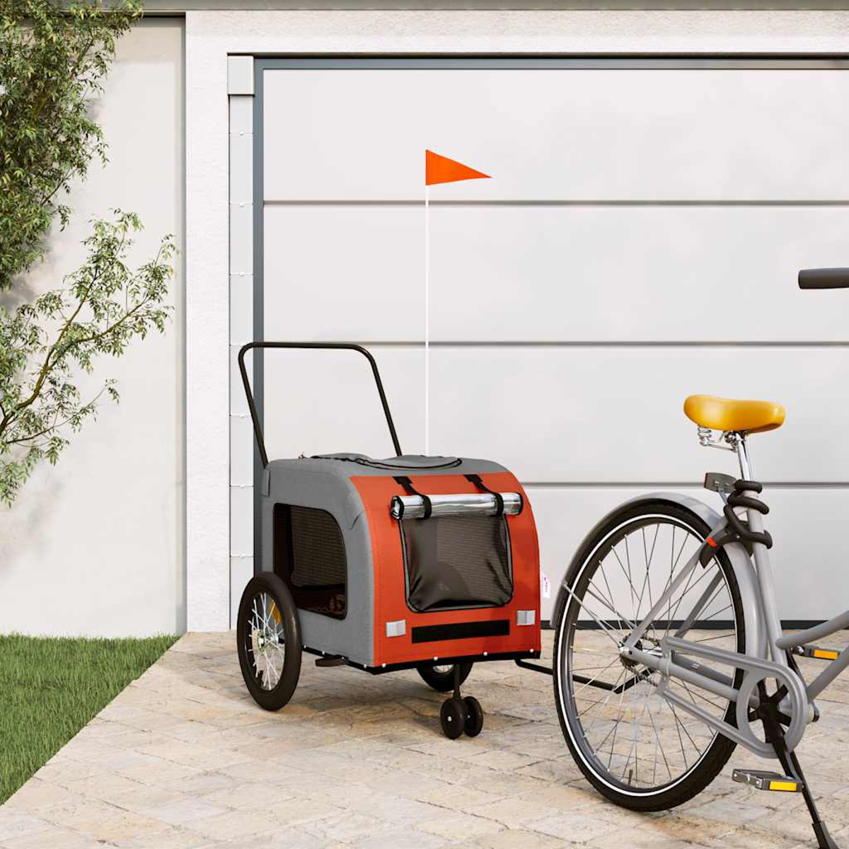 Ein grauer und oranger Haustieranhänger ist vor einer Garage an ein Fahrrad angehängt.