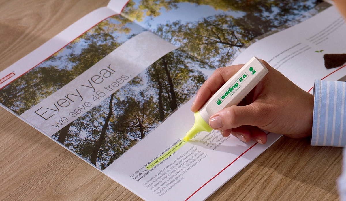 Una mano usa un evidenziatore giallo su una rivista con testo sul salvataggio degli alberi.