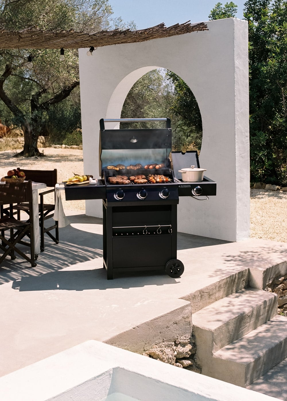 Una parrilla negra con comida cocinándose, al aire libre bajo un toldo.