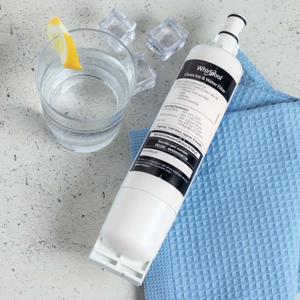 Whirlpool Eis- und Wasserfilter neben einem Glas Wasser und Eiswürfeln auf grauem Untergrund.