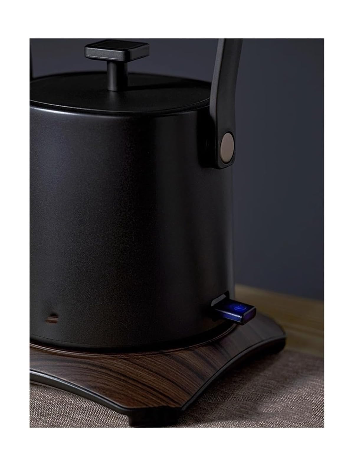 Eine schwarze Teekanne mit Holzsockel und blauem Lichtschalter.