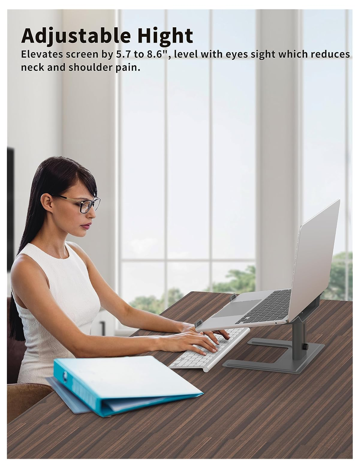 Eine Frau sitzt an einem Holztisch und tippt auf einer Tastatur, daneben ein Laptopständer.