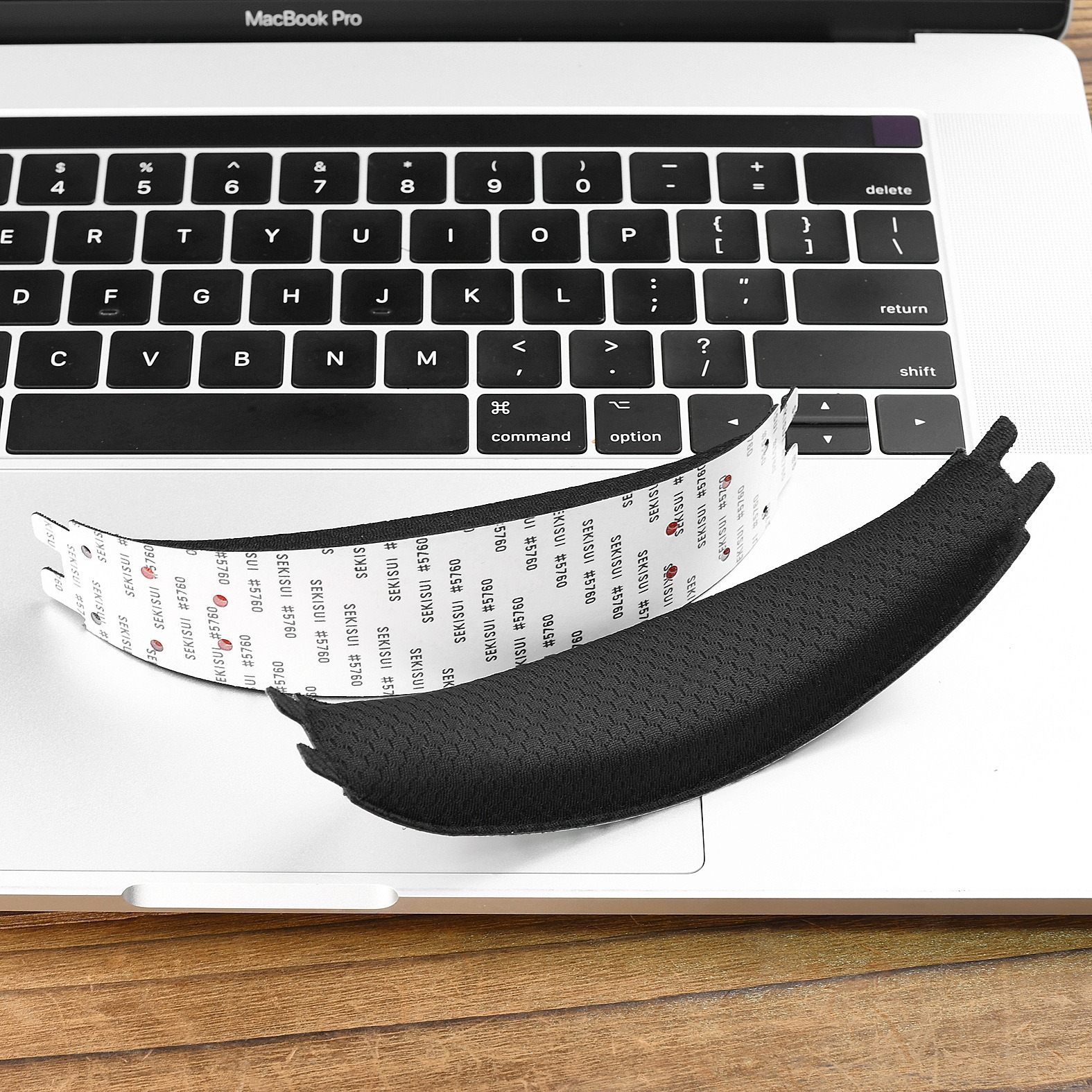 Schwarzes Polsterteil auf einer geöffneten MacBook Pro Tastatur mit Klebeband.