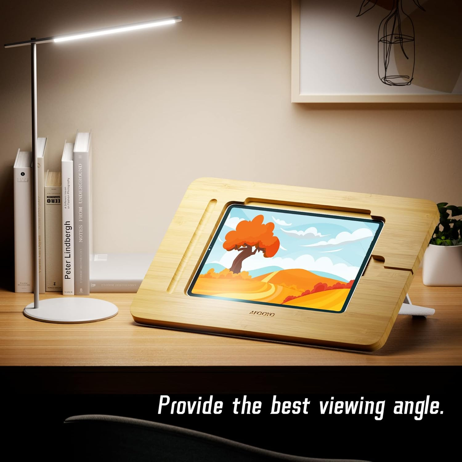 Ein hölzerner Tabletständer mit einer farbenfrohen Landschaft auf dem Bildschirm, nahe Büchern und einer Lampe.