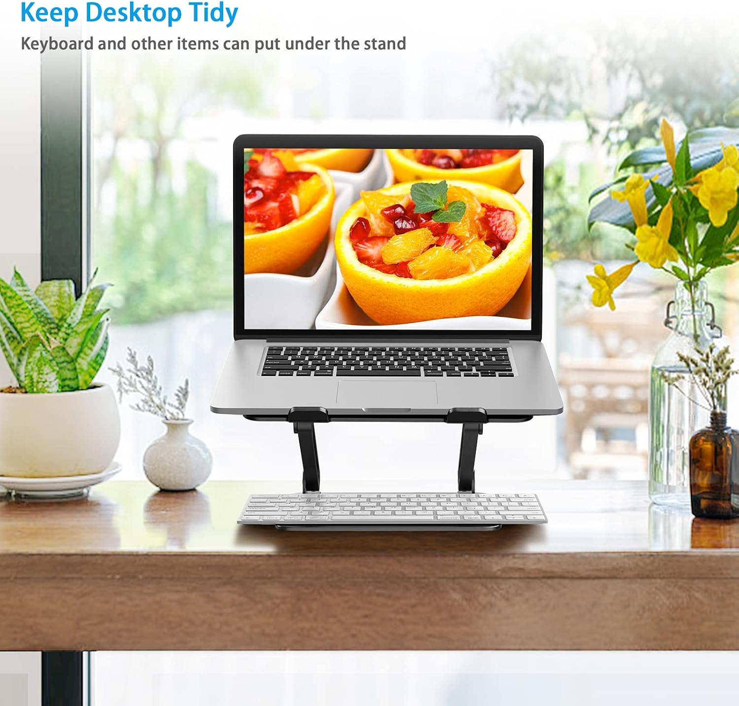 Ein Laptop steht auf einem Ständer über einer Tastatur, daneben Pflanzen und Blumen.