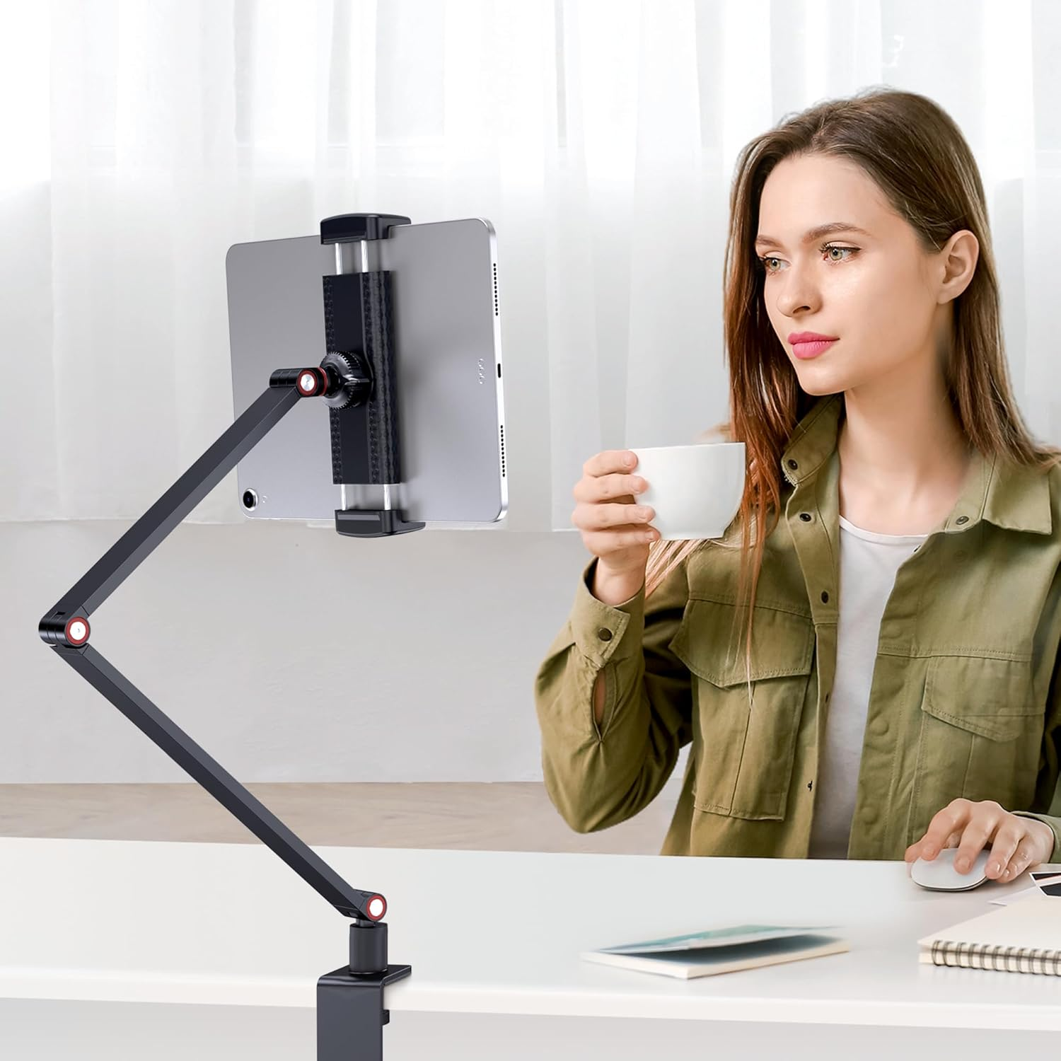 Frau trinkt Kaffee neben Tablet auf Ständer. Schreibtisch mit Maus und Notizbuch.