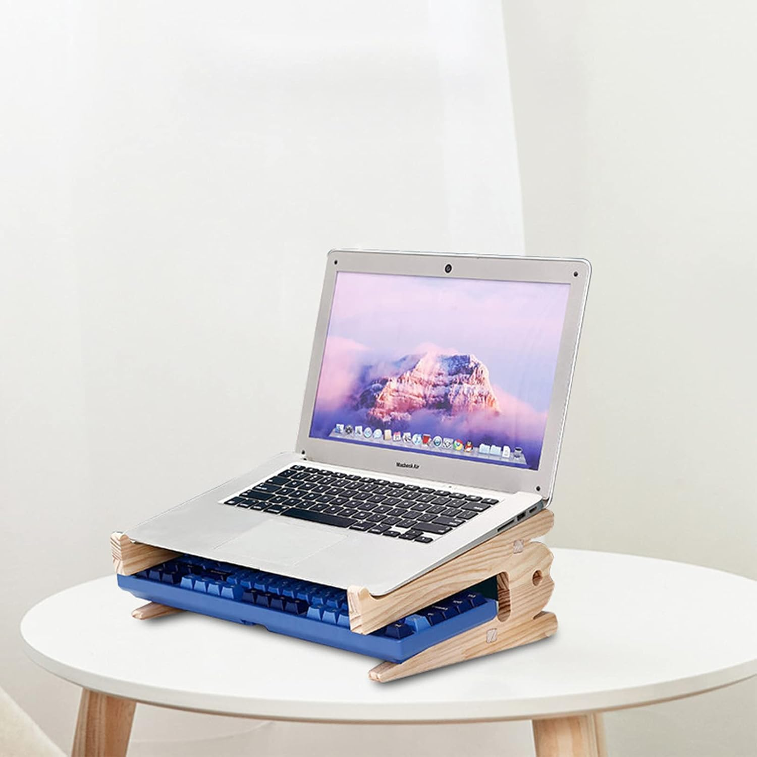 Ein Laptop steht auf einem Holzständer mit einer blauen Tastatur darunter auf einem weißen Tisch.