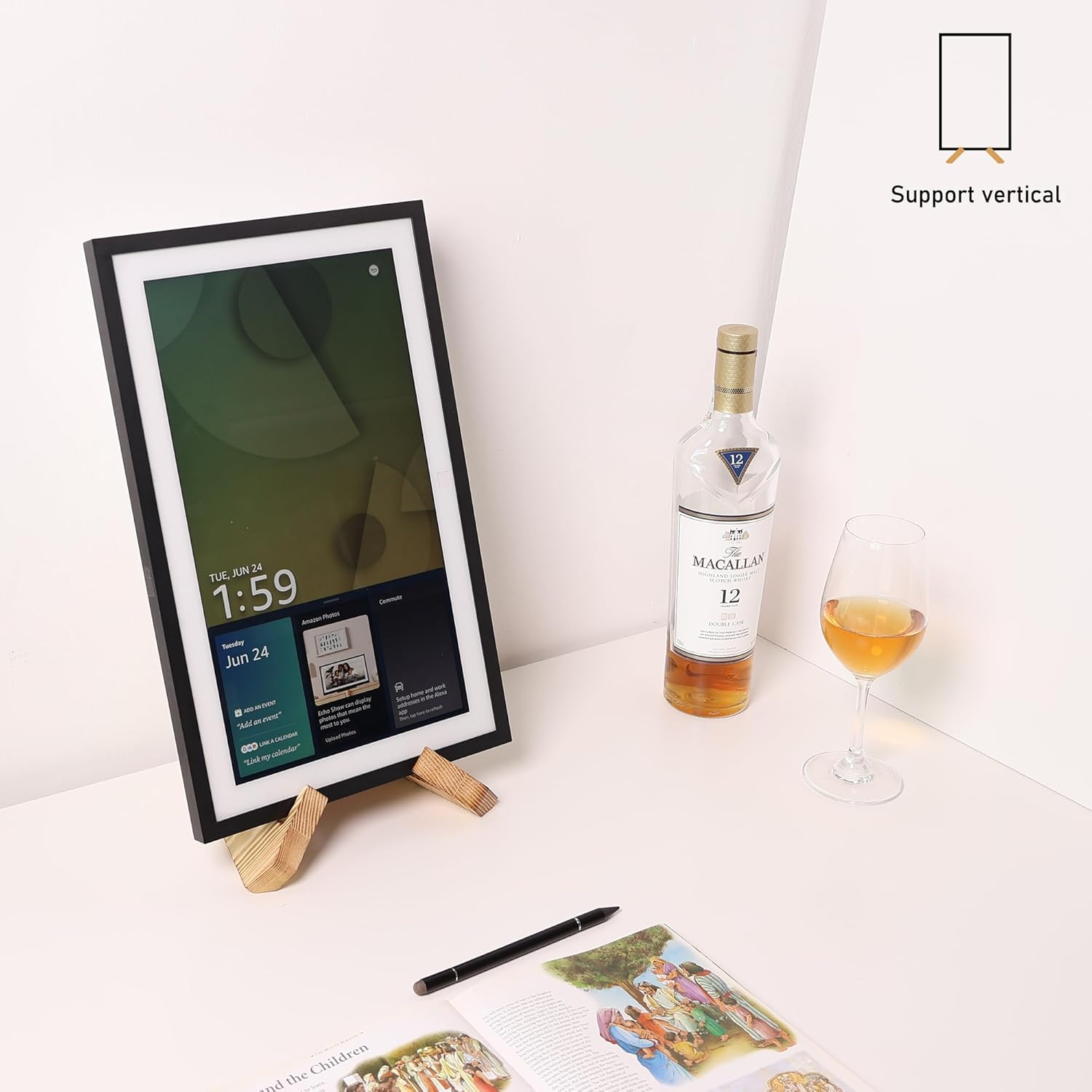 Ein digitaler Bilderrahmen mit schwarzem Rahmen steht auf einem Holzständer, daneben eine Whiskyflasche und ein Glas.